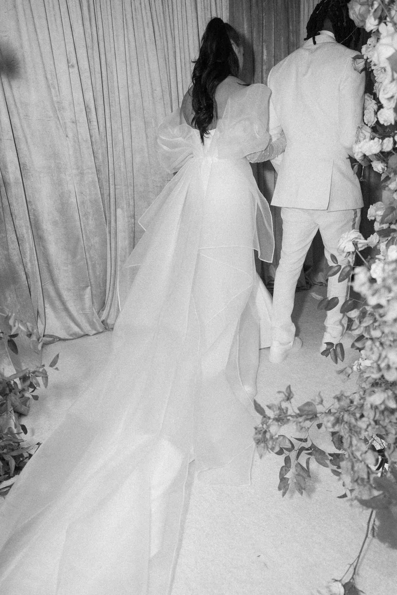 black and white photo of bride and groom walking away in flower hallway