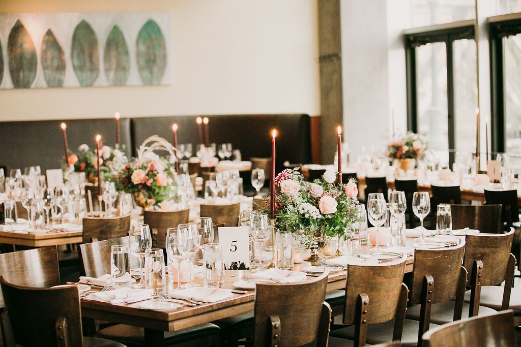 Wedding reception with wooden tables and chairs, taper candles, and pink flower arrangements at Coohills restaurant